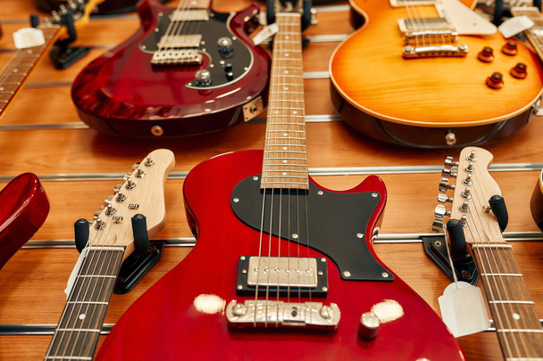 Κοντινό πλάνο με κόκκινες χορδές κιθάρας σε ένα κατάστημα μουσικών οργάνων. Πολλές διαφορετικές κιθάρες προς πώληση. Χόμπι και αναψυχή. - Φωτογραφία, εικόνα