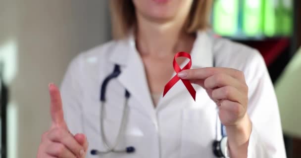 Czerwona wstążka HIV w rękach lekarza w klinice. Symbol świadomości charytatywnej i wsparcia w chorobie - Materiał filmowy, wideo