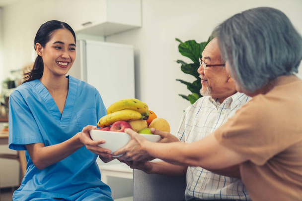 Contented senior couple taking a bowl of fruit from a nurse at home. Senior care at home. - Photo, Image