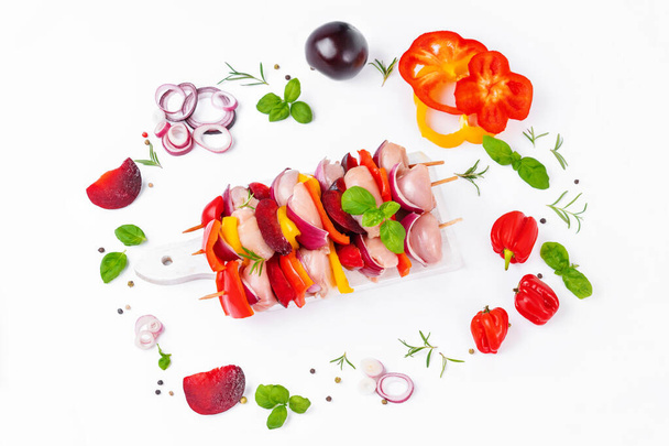 Skewers with pieces of raw meat, red, yellow and green pepper.Top view.Raw chicken leg meat skewers with vegetables,plums,peppers,onions, on a white background.Uncooked mixed meat skewer with peppers. - Foto, afbeelding
