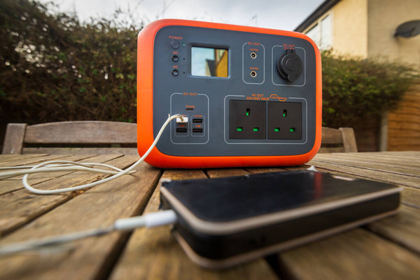 Portable power station solar electricity generator outdoors with mobile phone plugged in to charge. Wireless charging lithium battery backup for power outage, emergencies, travel or camping. - Foto, Imagem
