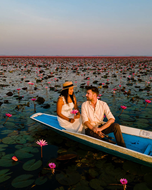 Sonnenaufgang am Meer aus rotem Lotus, Lake Nong Harn, Udon Thani, Thailand. Paar Männer und Frauen in einem Holzboot während des Sonnenaufgangs am Roten Lotussee in Thailand - Foto, Bild