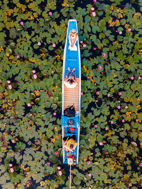 Рассвет в море красного лотоса, озеро Нонг Харн, Удон Тани, Таиланд. Пара мужчин и женщин в деревянной лодке во время восхода солнца на озере Красный Лотос в Таиланде - Фото, изображение