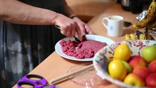 Using a metal spoon to break apart a block of minced beef on a plate on top of a kitchen work surface - Materiał filmowy, wideo