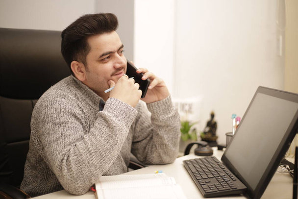 Um jovem empresário está sentado na cadeira e falando no celular no escritório. - Foto, Imagem