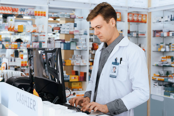 Portrait of male pharmacist using computer checking medicine or medical supply storage at counter in pharmacy. Inventory work in qualified chemist shop drugstore concept. - Photo, Image