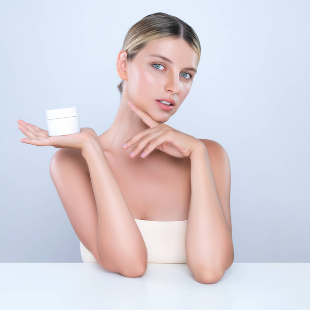 Intrygujący piękny idealny kosmetyk kobieta portret trzymać krem mockup słoik lub krem nawilżający do pielęgnacji skóry, anti-aging produktu w izolowanym tle. Naturalna koncepcja zdrowego modelu skóry. - Zdjęcie, obraz