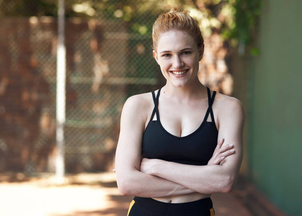 Bringing her confidence to the court. Cropped portrait of an attractive young female athlete standing with her arms folded on the basketball court - Foto, Imagen
