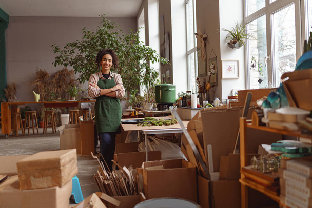 Attractive smiling florist stands on background of her own floral decor studio and looking at camera - Foto, immagini