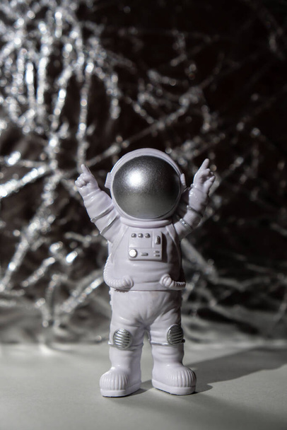 Plastic speelgoed figuur astronaut op zilveren achtergrond Kopieer ruimte. Concept van reizen buiten de aarde, particuliere ruimtevaarder commerciële vluchten. Ruimtemissies en duurzaamheid - Foto, afbeelding