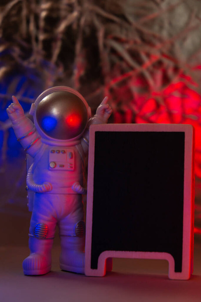 Πλαστική φιγούρα παιχνίδι αστροναύτης με κόκκινο και μπλε φως Μαύρο πίνακα με Copy χώρο για το κείμενό σας. Έννοια της εκτός γης ταξίδια, ιδιωτικές διαστημικές εμπορικές πτήσεις. Διαστημικές αποστολές και βιωσιμότητα - Φωτογραφία, εικόνα