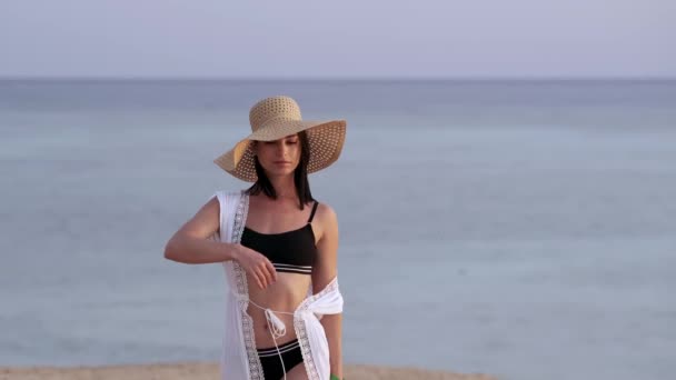 Bella ragazza con cappello di paglia godendo prendere il sole sulla spiaggia. Viso ravvicinato di giovane abbronzata dagli occhi chiusi che si gode la brezza del mare. Carefree bella donna sorridente con l'oceano - Filmati, video