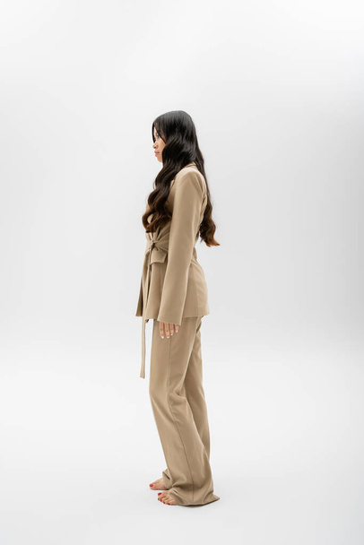 longitud completa de descalzo modelo asiático en traje de moda de pie sobre fondo gris - Foto, Imagen