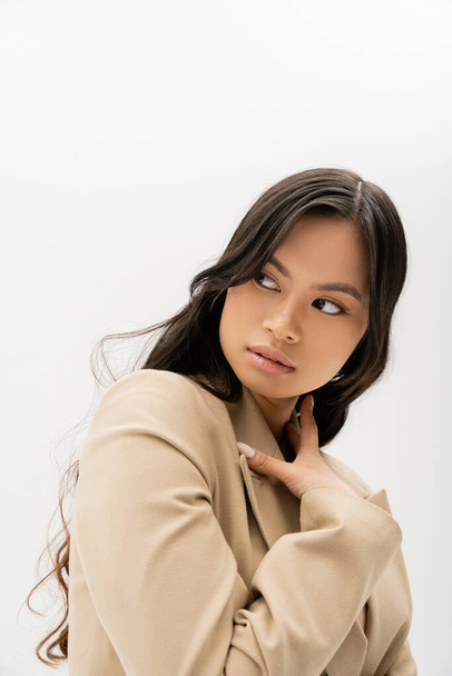 Uzun esmer saçlı, bej ceketli ve gri renkli gözlerden uzak Asyalı bir kadının portresi. - Fotoğraf, Görsel