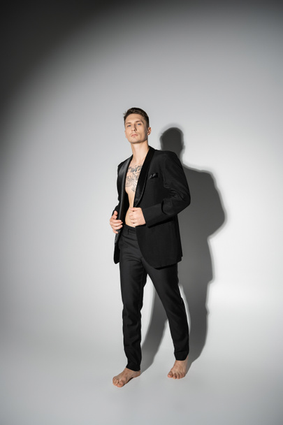 full length of barefoot man in black elegant suit standing on grey background with shadow - Foto, Imagem