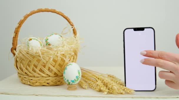 Easter holiday phone show thumb up empty space for advertising In basket eggs with embroidered pattern ribbon embroidery on eggshells wheat spikelets on table place for dough close-up basket - Filmmaterial, Video