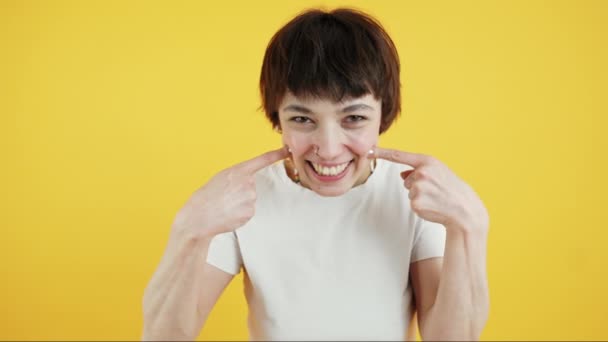 Adorable positive young adult girl looking at camera and touching her dimples with a smile. Medium closeup shot. Yellow background. High quality 4k footage - Imágenes, Vídeo