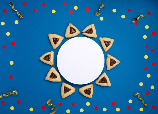 Homemade Purim hamantaschen cookies, Triangular pastry, Carnival mask, noisemaker, sweet candies and festive party decor on dark blue background, Top view. Purim celebration jewish holiday concept. - Photo, Image