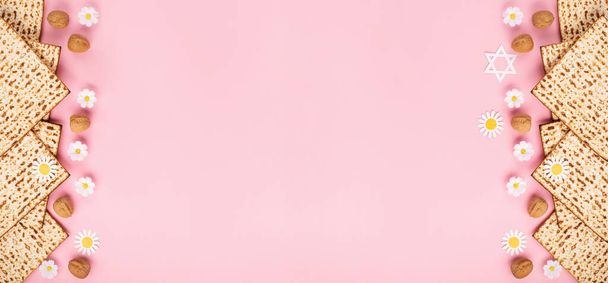 Żydowskie święto Koncepcja karty okolicznościowej Pascha z matą, orzechami i kwiatami stokrotki na różowym tle. Seder Pesach wiosna wakacje tło, widok z góry, przestrzeń do kopiowania. - Zdjęcie, obraz