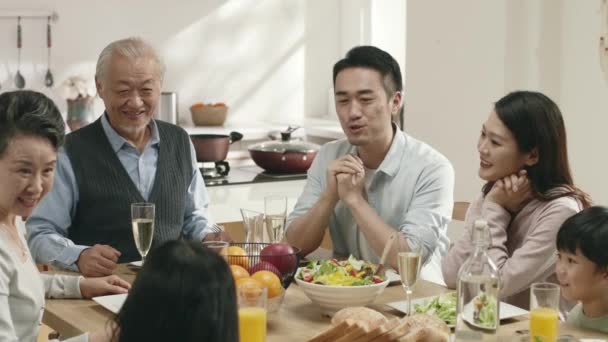 three generation asian family sitting at dining table having a pleasant conversation while eating meal - Filmati, video