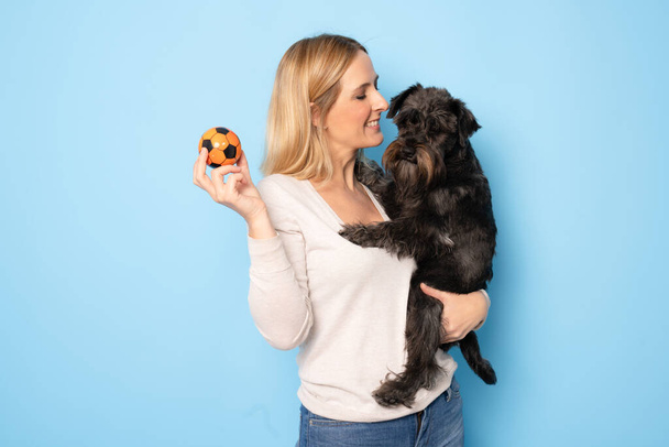 Χαριτωμένη νεαρή γυναίκα αγκαλιάζει κουτάβι της schnauzer σκυλί. Αγάπη μεταξύ ιδιοκτήτη και σκύλου. Απομονωμένο σε μπλε φόντο. Πορτρέτο στούντιο. - Φωτογραφία, εικόνα
