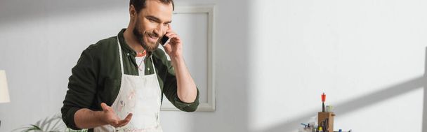Carpintero sonriente en delantal hablando en smartphone en taller, pancarta  - Foto, Imagen