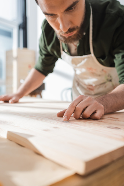 Carpenter in blurred apron touching surface of wooden board  - 写真・画像