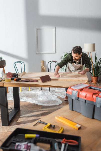 Artesano lijado tablero de madera cerca de herramientas borrosas en el taller  - Foto, imagen