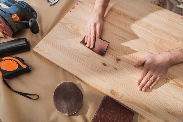 Κάτοψη του ξυλουργού λείανση ξύλινη σανίδα κοντά σε εργαλεία στο τραπέζι  - Φωτογραφία, εικόνα