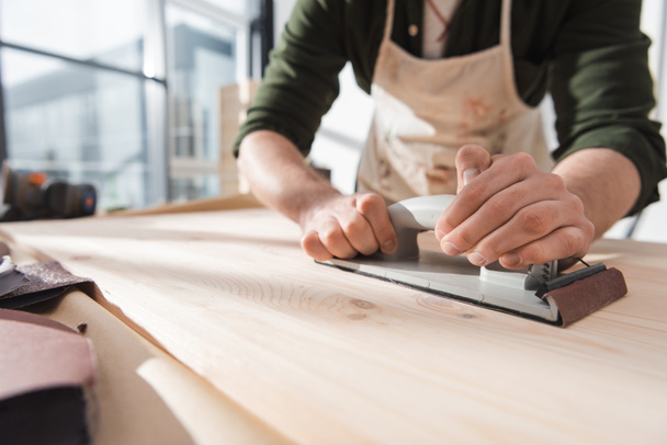 Cropped view of blurred workman sanding surface of wooden board  - Fotografie, Obrázek