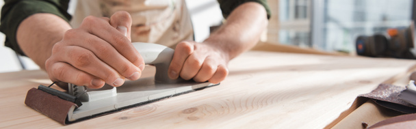 Cropped view of man in blurred apron sanding wooden board in workshop, banner  - Photo, Image