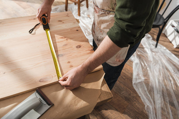 Vue grand angle du menuisier dans le tablier mesurant la planche en bois dans l'atelier  - Photo, image