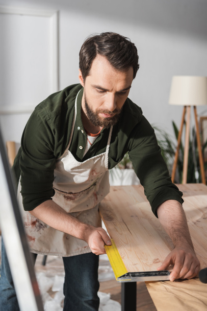 Bearded carpenter using square tool on wooden board in workshop  - Valokuva, kuva