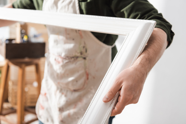 Cropped view of blurred restorer in apron holding wooden picture frame  - Foto, afbeelding