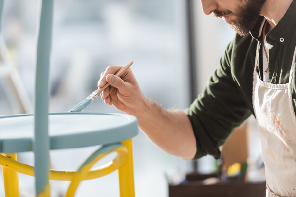 Cropped view of craftsman in apron repainting chair in workshop  - Zdjęcie, obraz