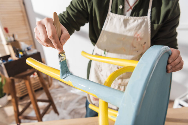Cropped view of craftsman painting on wooden chair in blurred workshop  - Fotografie, Obrázek