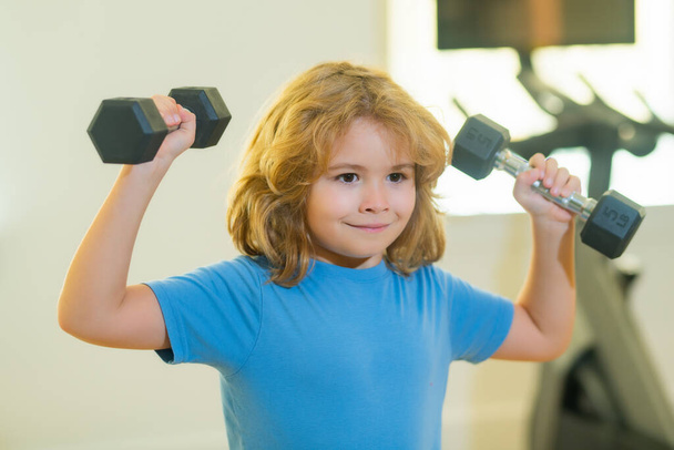 Dítě cvičí v tělocvičně. Sportovní aktivity ve volném čase s dětmi. Chlapec drží činky - Fotografie, Obrázek