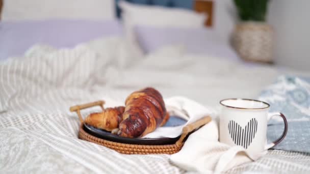 朝食、居心地の良い、朝、休日や冬のコンセプト-自宅でベッドで木製のボード上のコーヒーとクロワッサンのカップ付きの居心地の良いベッドルーム - 映像、動画