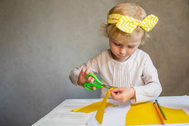 Una niña pequeña se dedica a la creatividad. El niño aprende a cortar el papel amarillo. El niño hace el trabajo para el Día de las Madres y el 8 de marzo - Foto, imagen