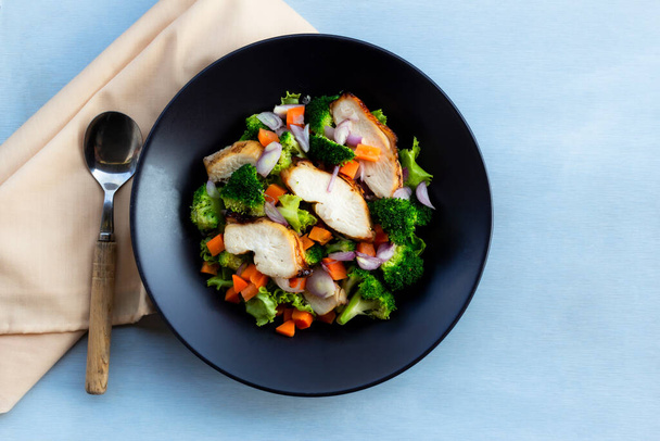 Куриный салат имеет овощи в черной миске на синем фоне дерева вид сверху, концепция здоровой пищи. - Фото, изображение