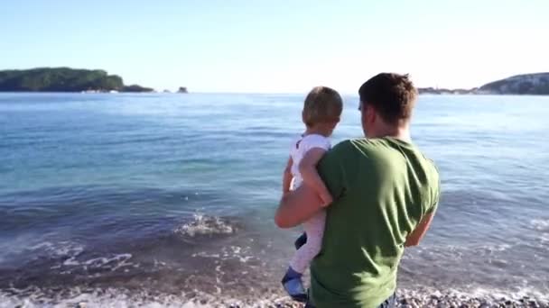 Dad with a little girl in his arms throws pebbles into the sea. High quality 4k footage - Video, Çekim