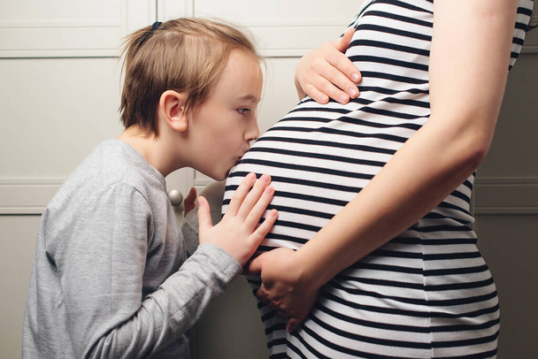 Child boy kissing his mother pregnant tummy. Pregnant mother and son hugging. Cute boy with mom spending time together at home. Child boy kissing his mother pregnant tummy. Pregnancy, family, parenthood, preparation and expectation concepts. - Fotografie, Obrázek