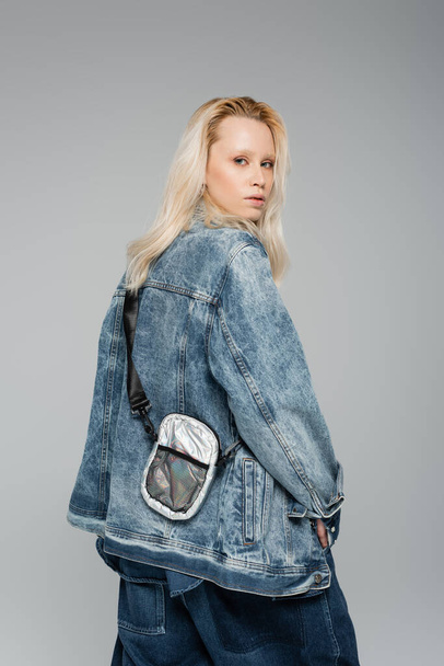 young blonde model in stylish denim jacket with belt bag posing isolated on grey  - Photo, Image