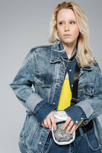 blonde albino model in stylish denim outfit with belt bag posing isolated on grey  - Foto, immagini