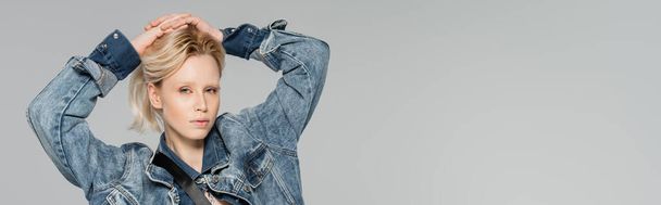 blonde woman in stylish denim jacket posing with hands on head isolated on grey, banner  - Foto, imagen