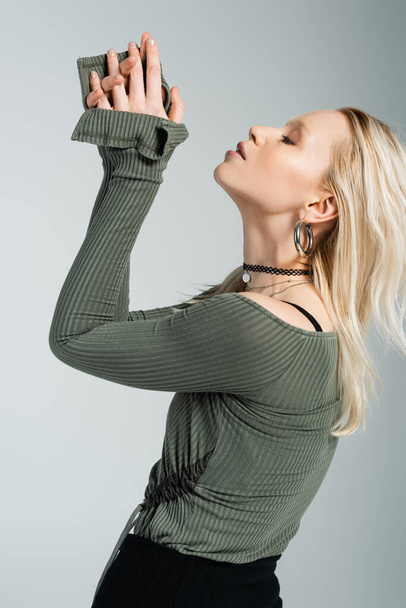 side view of blonde woman in long sleeve shirt and black skirt posing isolated on grey  - Fotografie, Obrázek