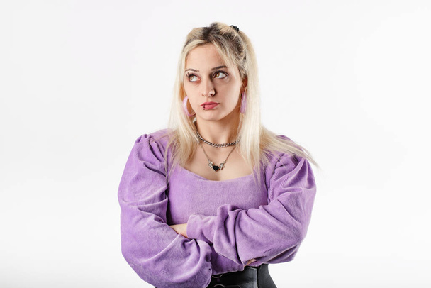 Portrait of young blonde woman wearing ribbed blouse standing isolated over white background with folded arms looks at the empty copy space with an expression of disapproval. - Foto, afbeelding