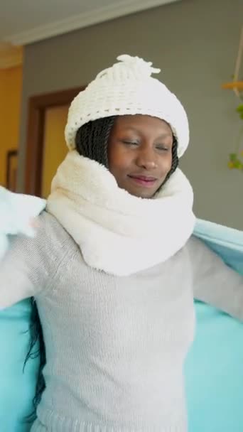 Young woman covering herself with a blanket to fight cold wave. Wearing winter clothes in a cozy living room. UHD Vertical video 4K - Imágenes, Vídeo