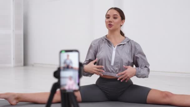 Young Girl Shooting Her Fitness Videoblog. Young Girl Conduct Remote Teaching to Training Online During Blogging. Girl Shooting a Video Blog While Doing Exercises of Stretching on Mat in Bright Room. - Video, Çekim