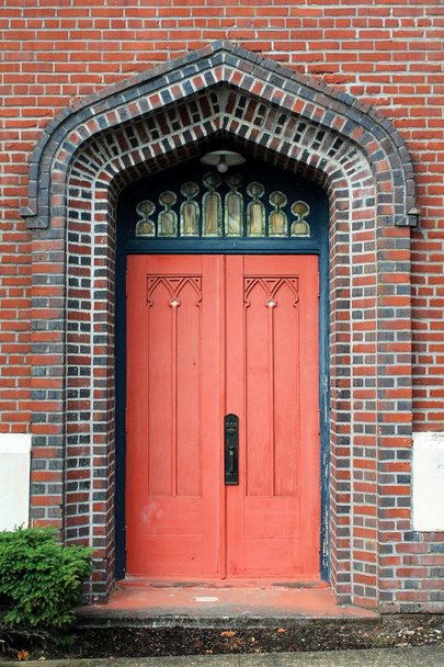 Ornate faded red door set in colorful brick wall - Photo, image